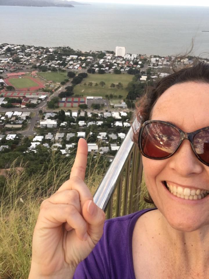 image of a woman atop a hill, smiling and pointing back towards the town below. 