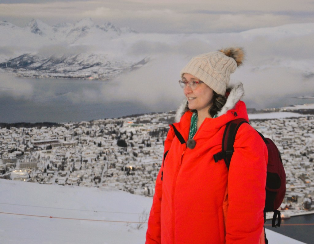 Image of woman wearing bright orange puffer jacket on snowy mountain in Norway