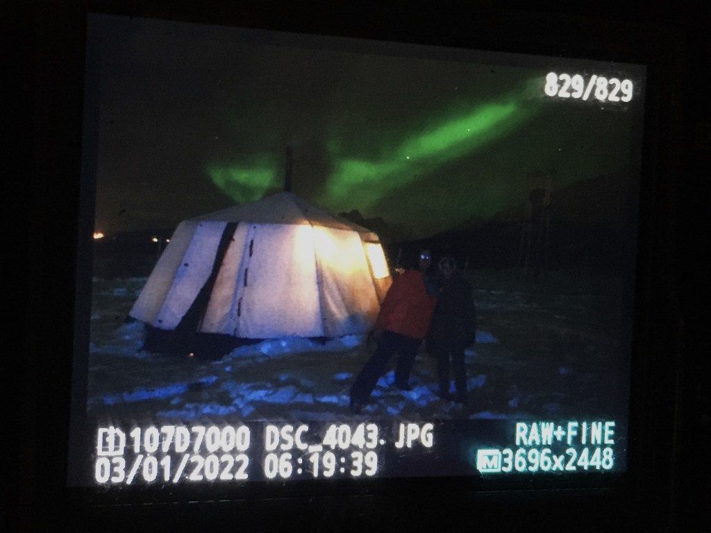 image of a camera showing an image of two people with the green northern lights. The camera display shows details of the camera settings