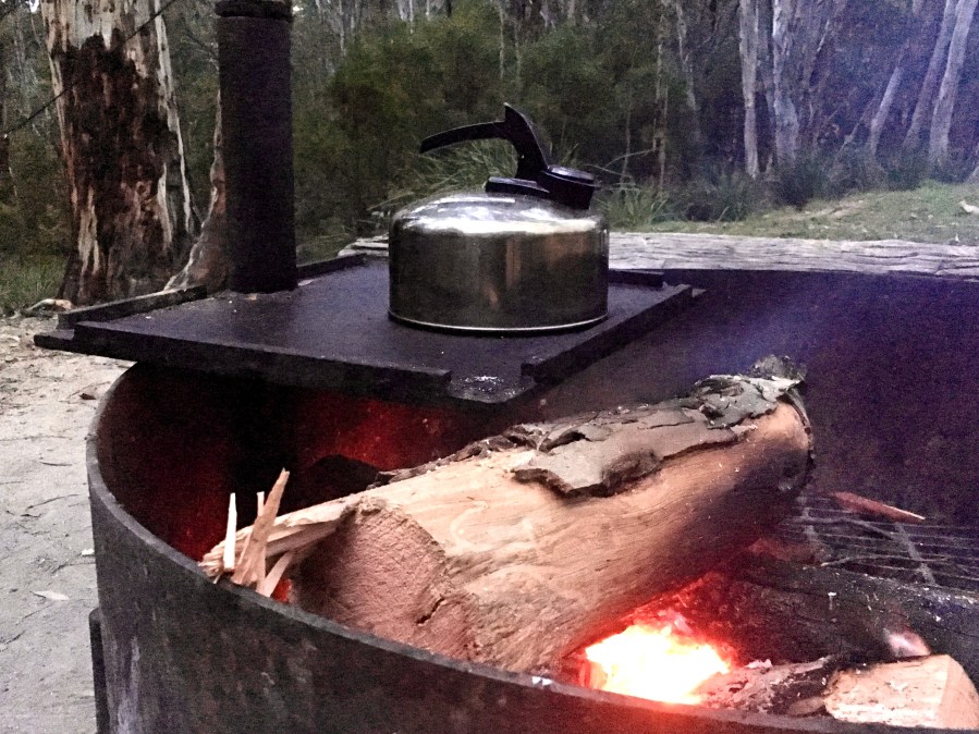 image of a camp kettle sitting over a fire pit outdoors 