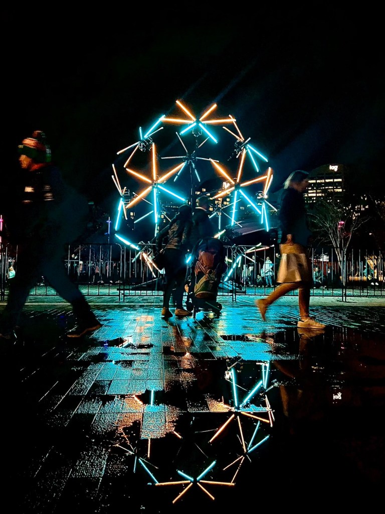 Image of teal and orange light sticks in a moving display during Vivid Sydney 2024