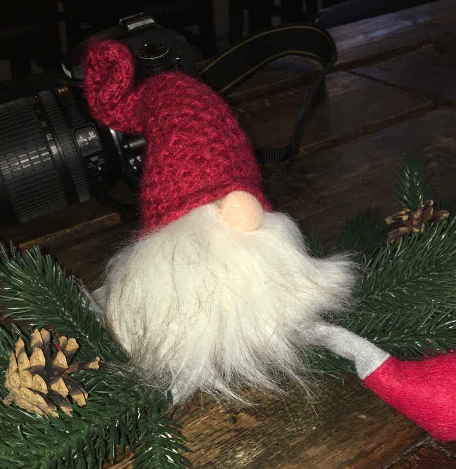 Image of small Norwegian toy gnome with red knitted hat sitting next to a camera