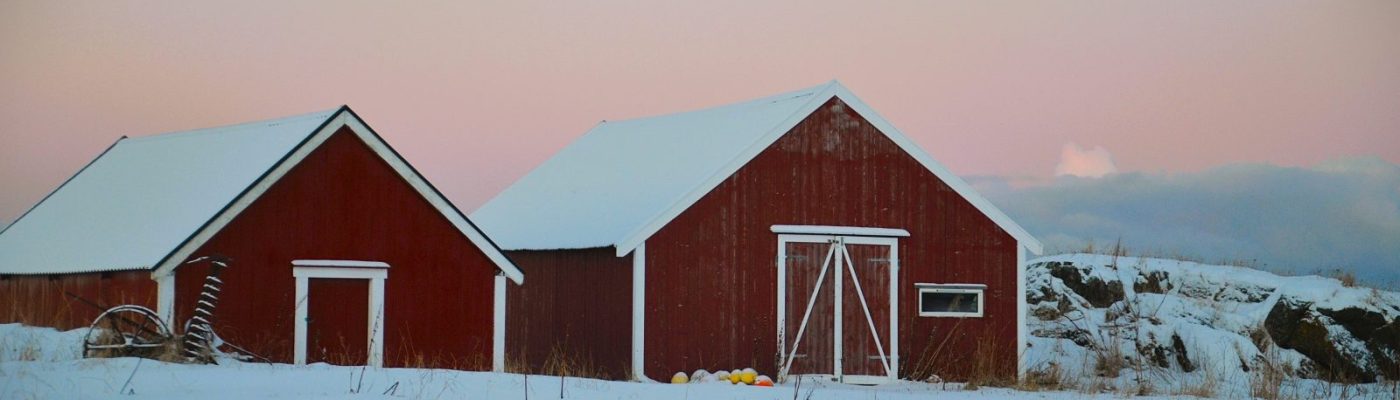image of Norwegian barn storage houses painted red with white trim set against stark white snow and a soft light peach sunrise
