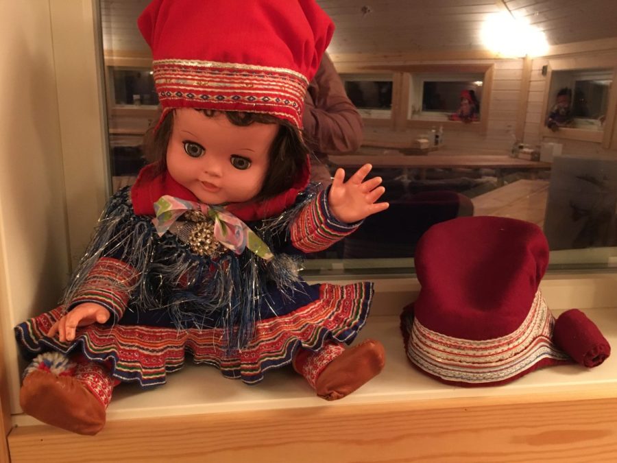 Image of a doll wearing traditional Sámi including a red hat and red trim