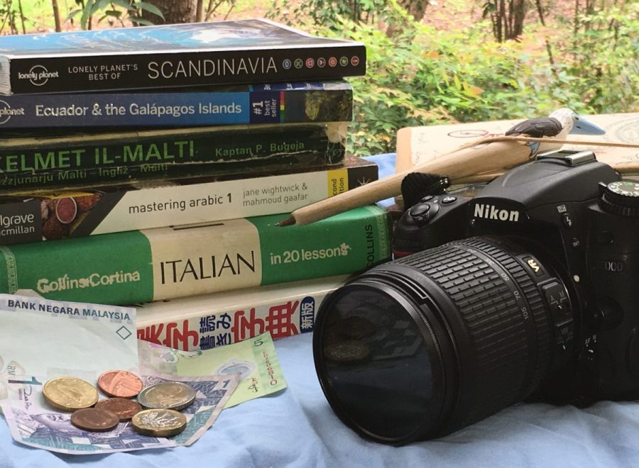 image of camera next to a stack of travel books, language books, and foreign currency